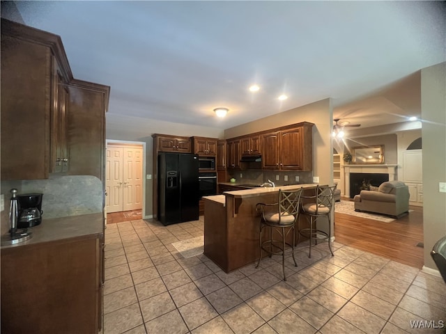 kitchen featuring a breakfast bar area, decorative backsplash, black appliances, and light wood-type flooring