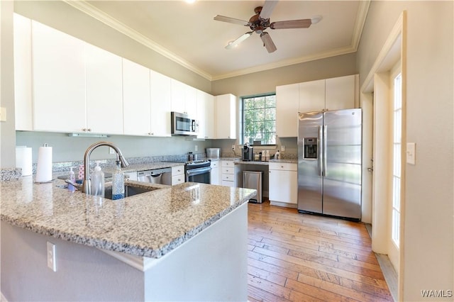 kitchen with white cabinets, a peninsula, light stone countertops, stainless steel appliances, and a sink