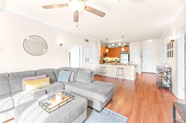 living room featuring light wood-style floors, ceiling fan, visible vents, and crown molding