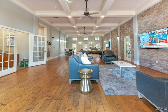 living area featuring coffered ceiling, ceiling fan, brick wall, wood finished floors, and beam ceiling