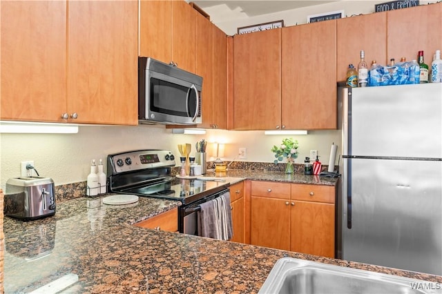 kitchen featuring appliances with stainless steel finishes, dark stone countertops, a sink, and brown cabinets