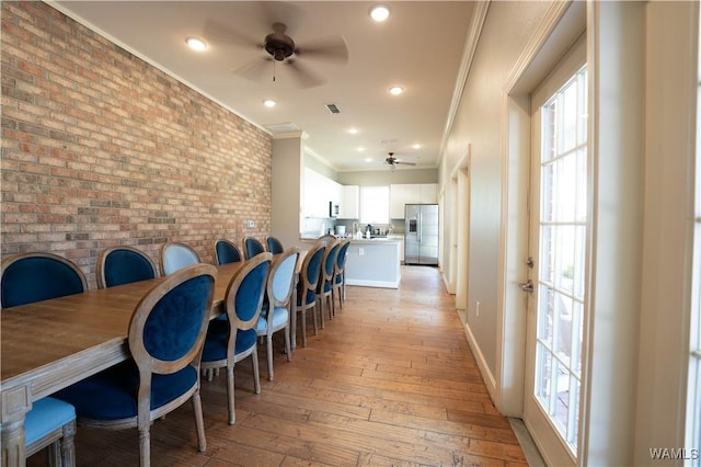 dining room with ornamental molding, light wood-type flooring, a healthy amount of sunlight, and brick wall