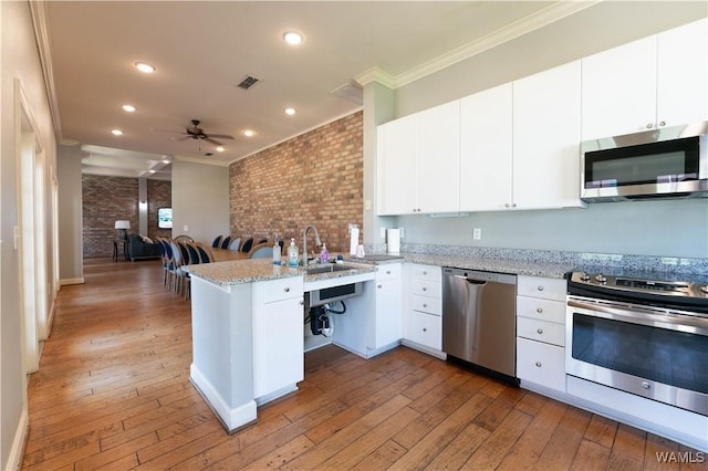 kitchen with light stone counters, a peninsula, visible vents, open floor plan, and appliances with stainless steel finishes