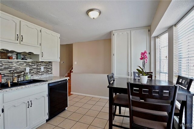 kitchen with light tile patterned floors, backsplash, white cabinets, a sink, and dishwasher