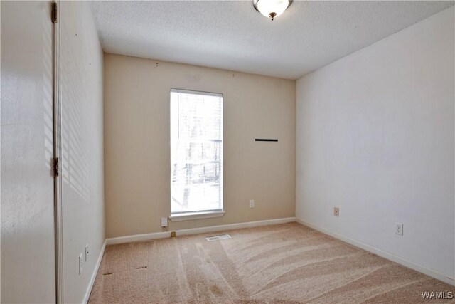 carpeted empty room with visible vents, plenty of natural light, a textured ceiling, and baseboards