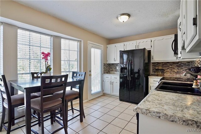 kitchen featuring light tile patterned floors, a sink, white cabinetry, black fridge, and backsplash