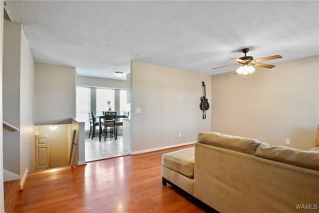 living area featuring ceiling fan, a textured ceiling, baseboards, and wood finished floors