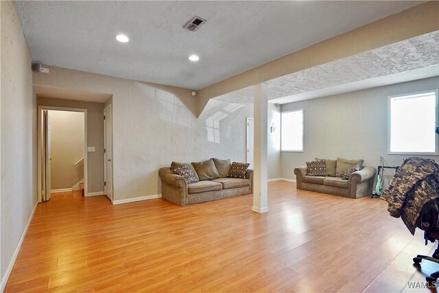 living area with light wood-type flooring, visible vents, baseboards, and stairs