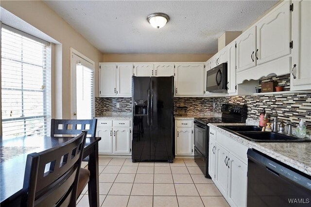 kitchen with light tile patterned floors, black appliances, a sink, and white cabinetry