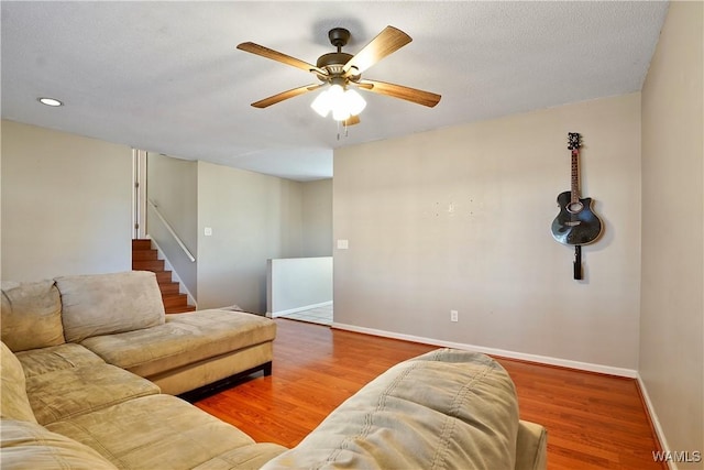 living area featuring a ceiling fan, a textured ceiling, baseboards, and wood finished floors