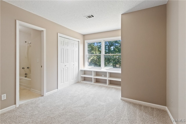 unfurnished bedroom with a textured ceiling, light carpet, and connected bathroom