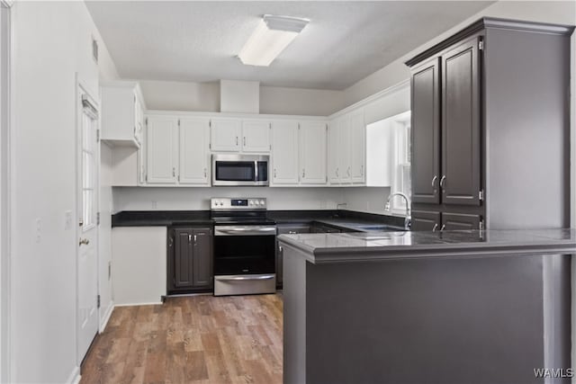 kitchen with kitchen peninsula, stainless steel appliances, sink, wood-type flooring, and white cabinets