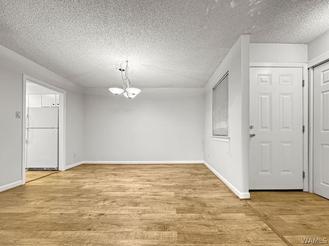 unfurnished dining area featuring a textured ceiling, an inviting chandelier, and light hardwood / wood-style floors