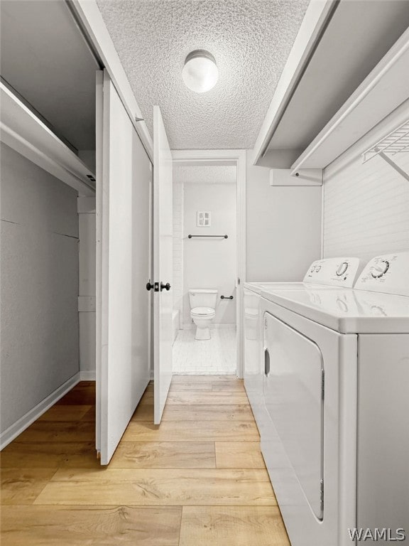 laundry room with washing machine and dryer, a textured ceiling, and light hardwood / wood-style flooring