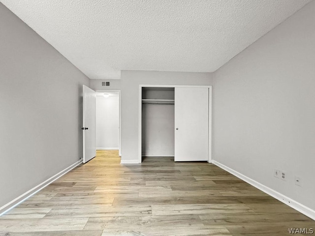 unfurnished bedroom featuring light wood-type flooring, a closet, and a textured ceiling