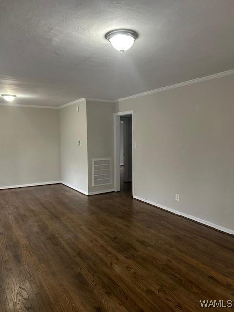 unfurnished room with dark wood-style floors, ornamental molding, visible vents, and baseboards