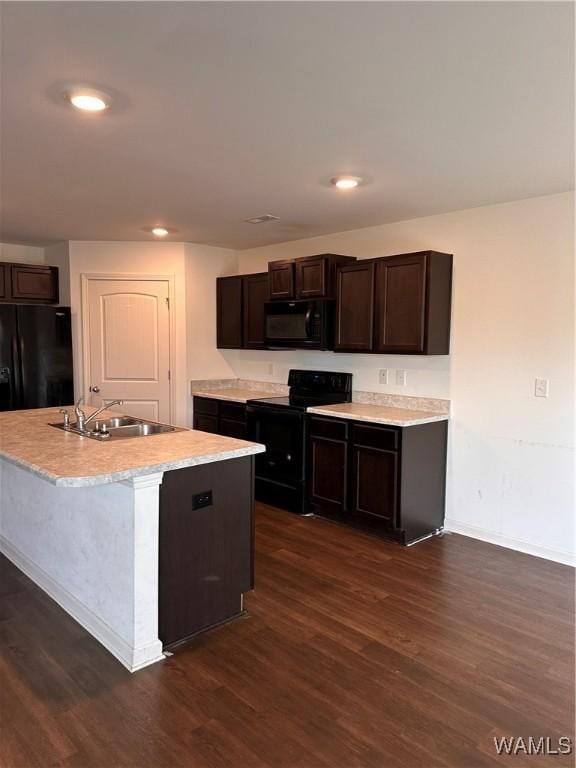 kitchen featuring dark brown cabinetry, sink, dark hardwood / wood-style flooring, an island with sink, and black appliances