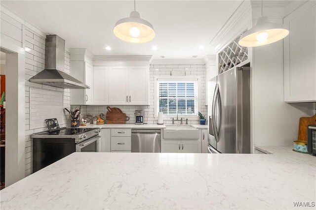 kitchen with white cabinets, wall chimney range hood, hanging light fixtures, light stone counters, and stainless steel appliances