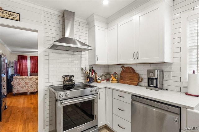 kitchen with white cabinets, appliances with stainless steel finishes, light wood-type flooring, and wall chimney exhaust hood