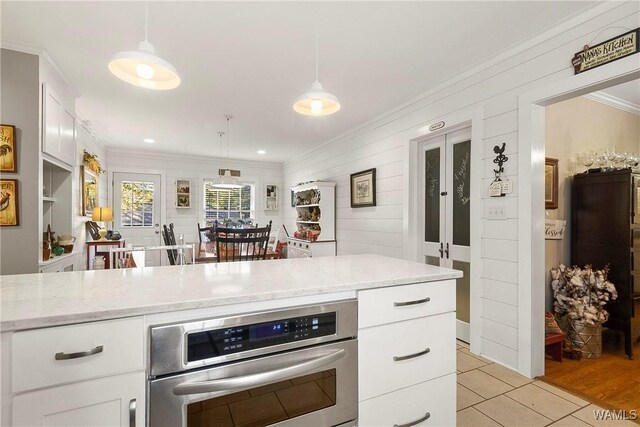 kitchen featuring white cabinets, decorative light fixtures, light stone counters, and stainless steel oven