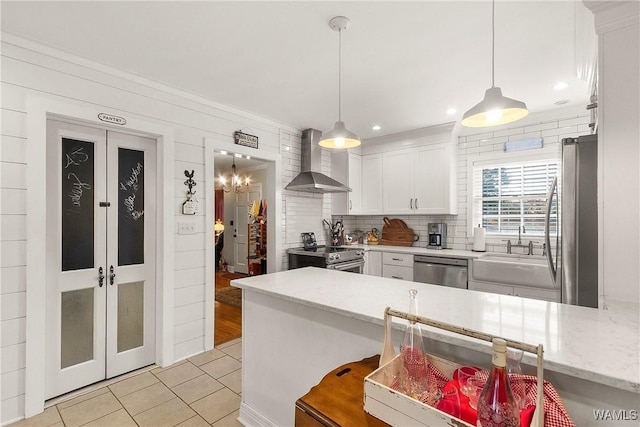 kitchen with white cabinets, appliances with stainless steel finishes, decorative light fixtures, and wall chimney range hood