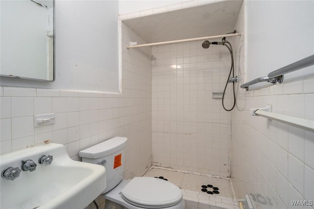 bathroom with sink, a tile shower, tile walls, and toilet