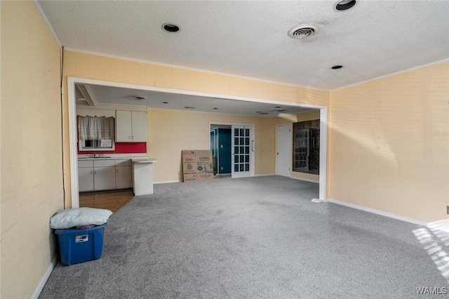 unfurnished living room featuring sink, crown molding, a textured ceiling, and carpet