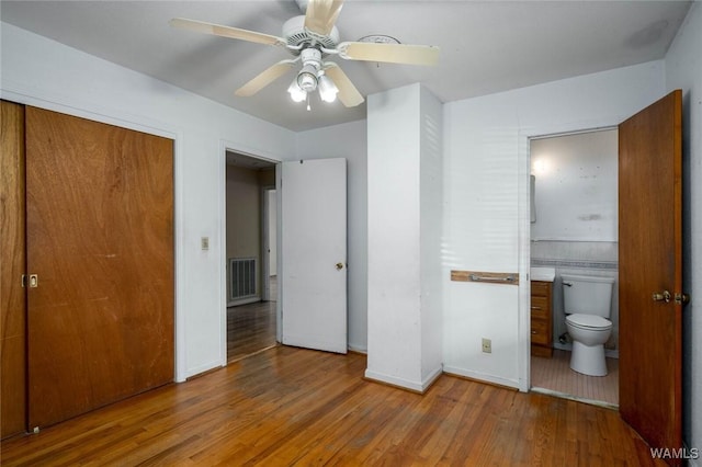 unfurnished bedroom featuring ceiling fan, wood-type flooring, connected bathroom, and a closet