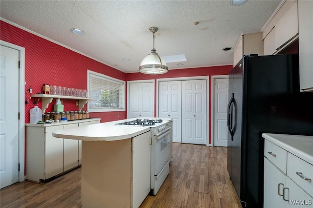 kitchen with hanging light fixtures, a center island, white cabinets, black fridge, and white gas stove