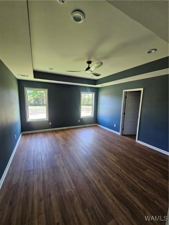 empty room featuring a ceiling fan, visible vents, a raised ceiling, baseboards, and dark wood-style floors