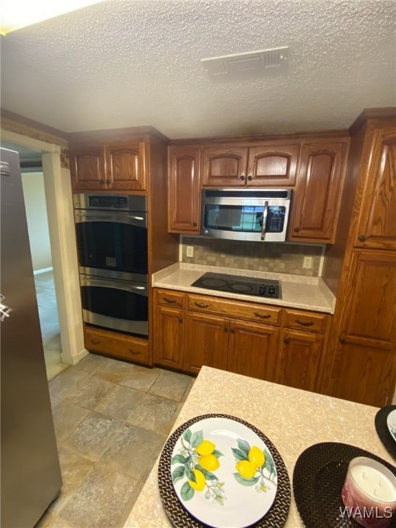 924 12th St SW, Fayette, AL 35555 - kitchen featuring appliances with stainless steel finishes, light countertops, brown cabinets, decorative backsplash, and light stone finish flooring