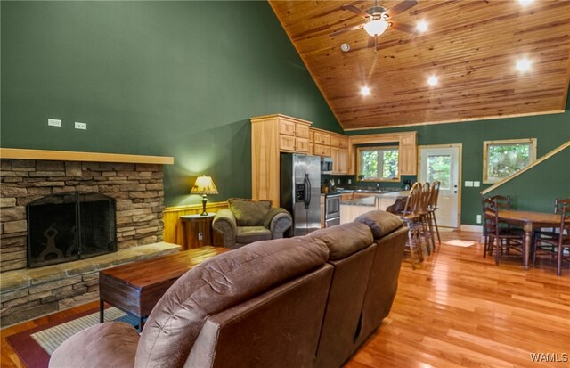 living room with light wood-type flooring, wood ceiling, ceiling fan, high vaulted ceiling, and a stone fireplace