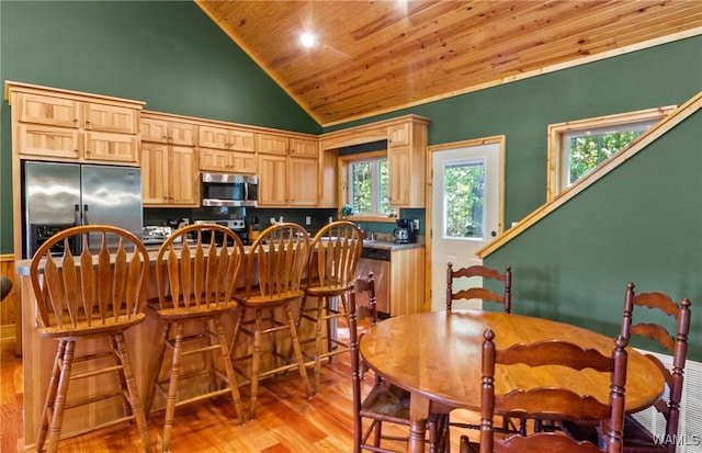 kitchen with stainless steel appliances, light hardwood / wood-style floors, light brown cabinetry, a breakfast bar, and wood ceiling