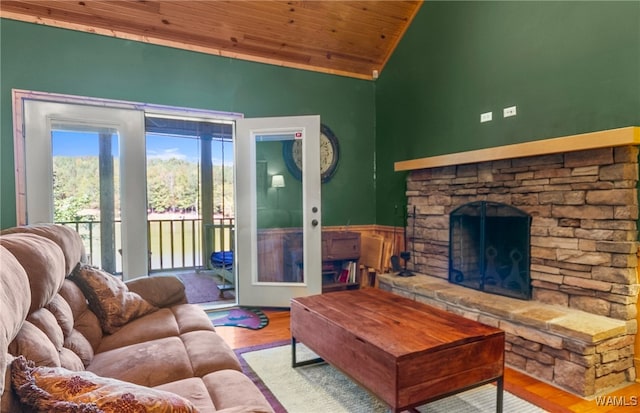 living room featuring high vaulted ceiling, light hardwood / wood-style flooring, wooden ceiling, and a stone fireplace