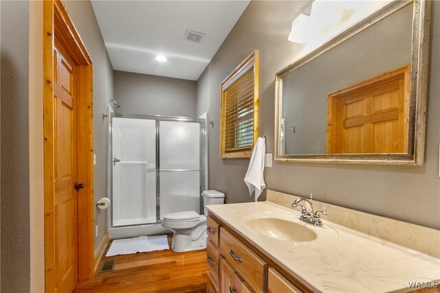 bathroom with toilet, vanity, a shower with shower door, and hardwood / wood-style flooring