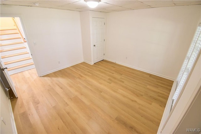 unfurnished bedroom featuring baseboards, light wood-type flooring, and a drop ceiling