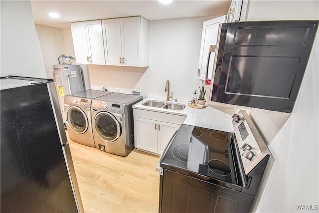 washroom with electric water heater, washing machine and clothes dryer, light wood finished floors, and a sink