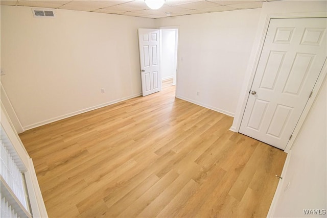 empty room featuring light wood-style flooring, baseboards, visible vents, and a drop ceiling