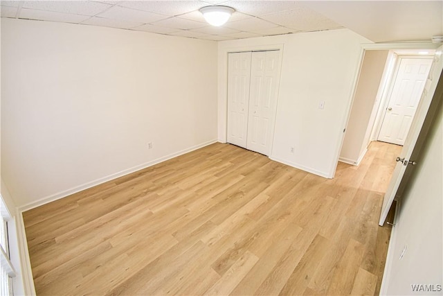 unfurnished bedroom featuring a paneled ceiling, baseboards, and light wood-style flooring