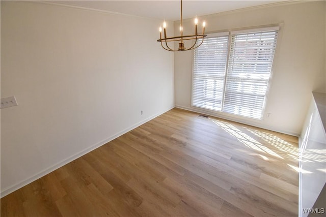 empty room featuring a notable chandelier, wood finished floors, visible vents, and baseboards