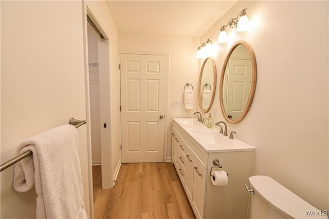 bathroom featuring double vanity, toilet, wood finished floors, and a sink