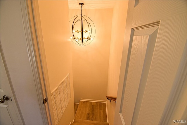 stairway with a notable chandelier, wood finished floors, and visible vents