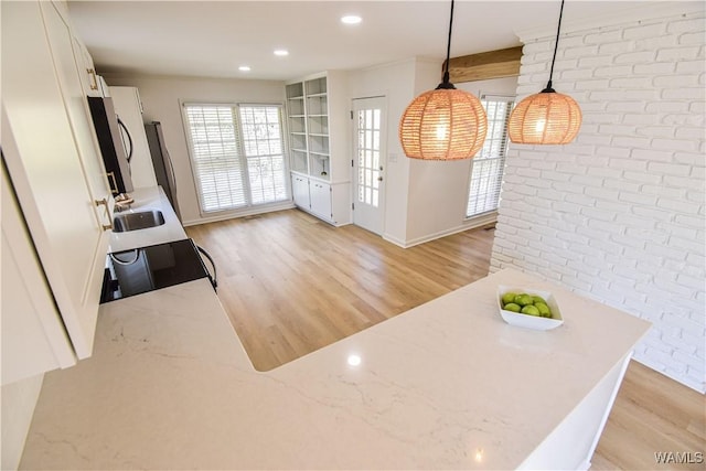 kitchen with light wood-style flooring, a sink, white cabinetry, brick wall, and stove