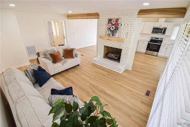 living area with a brick fireplace, recessed lighting, visible vents, and light wood-type flooring