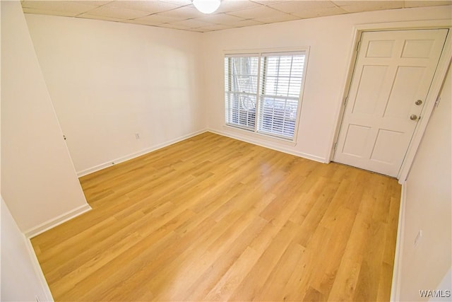 unfurnished room with light wood-type flooring, a drop ceiling, and baseboards