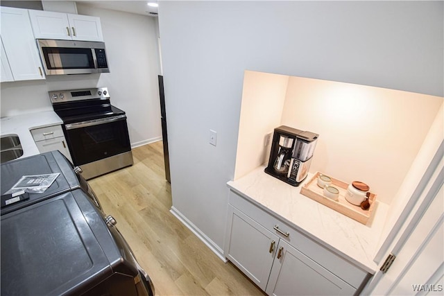 kitchen featuring light wood finished floors, white cabinets, appliances with stainless steel finishes, and baseboards