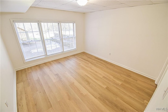 empty room with a drop ceiling, light wood-style flooring, and baseboards