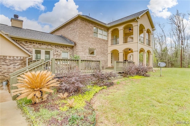 view of front of home with a front yard, brick siding, ceiling fan, and a balcony