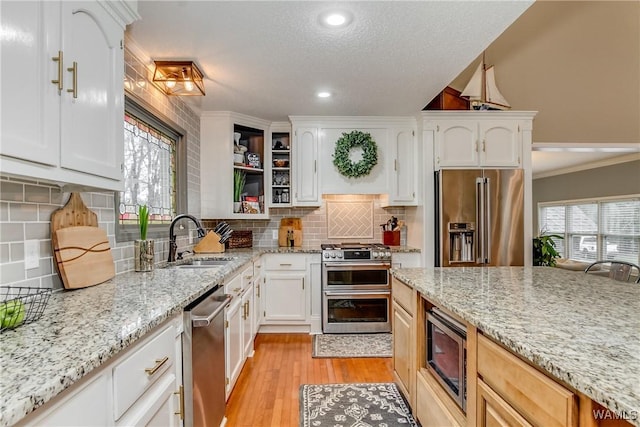 kitchen featuring light wood finished floors, plenty of natural light, high end appliances, and a sink