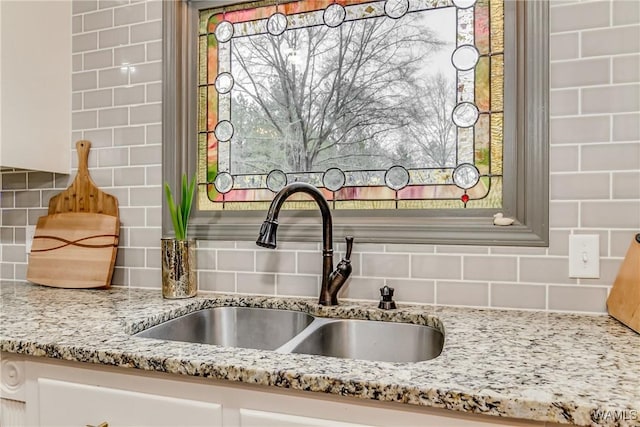 details featuring white cabinets, a sink, decorative backsplash, and light stone countertops